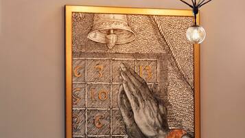 A framed artwork of praying hands on a wall, a modern chandelier, and a sofa with cushions.