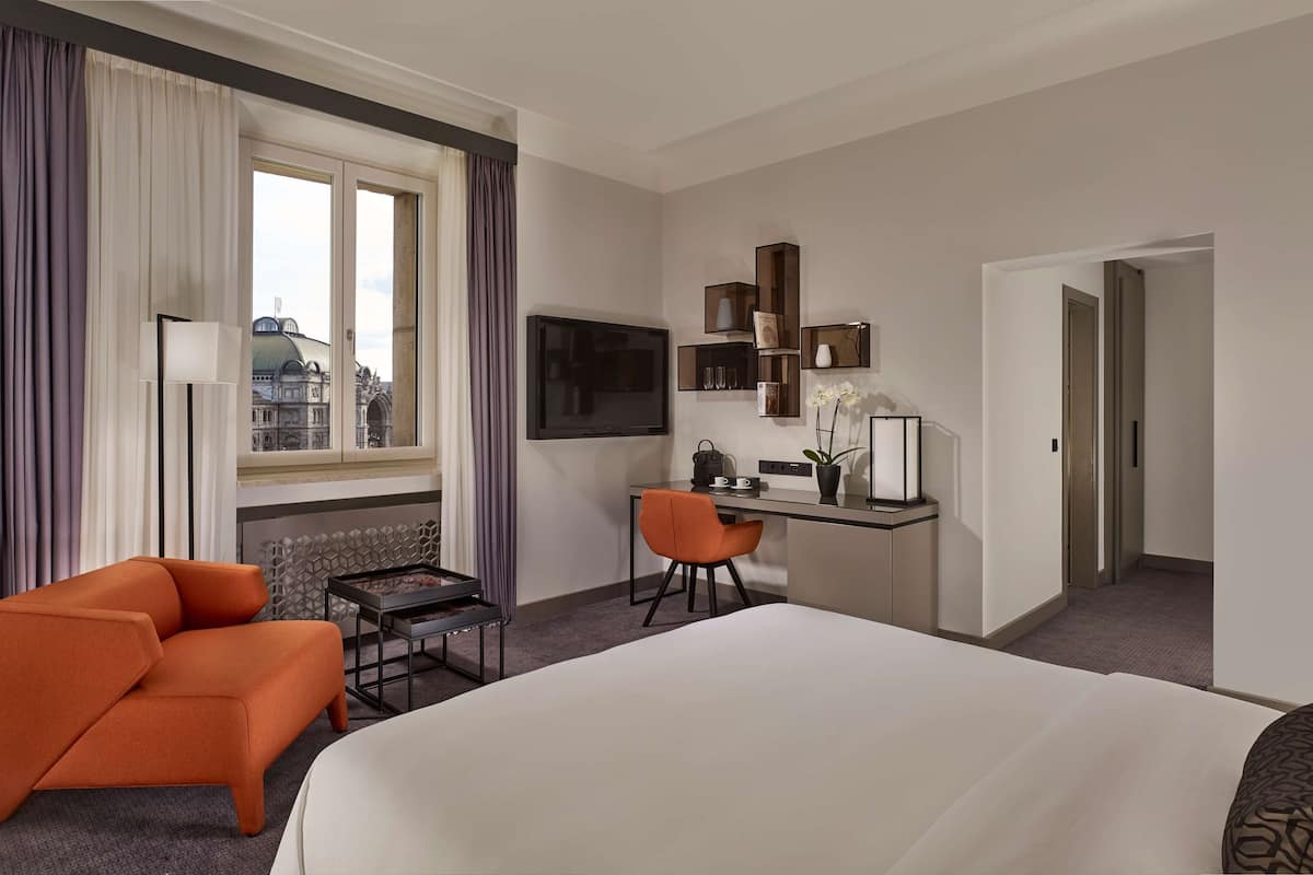 Ein Hotelzimmer mit einem großen Bett, einem Schreibtisch mit Stuhl, einem Fernseher und einem Fenster mit Vorhängen.