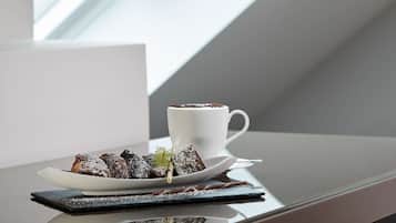 Een nagerechtbord met poedersuiker, een witte koffiekop en een takje groen op een reflecterend oppervlak.