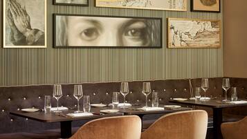 Un interior de restaurante con una larga mesa de comedor dispuesta para seis personas, cabinas tapizadas y obras de arte enmarcadas en las paredes.