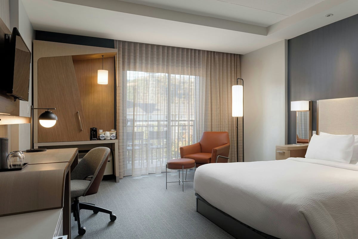 Ein Hotelzimmer mit einem großen Bett, einem Schreibtisch, einem Sessel, einem Fernseher und einem Fenster mit Vorhängen.