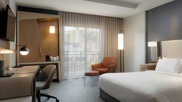 A hotel room with a large bed, a desk, a chair, a TV, and a window with curtains.