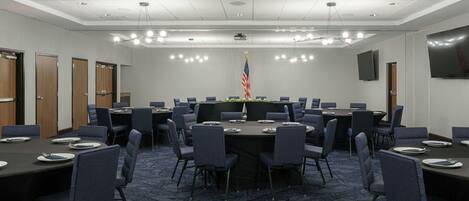 A conference room with a large oval table, multiple chairs, and a projector screen.