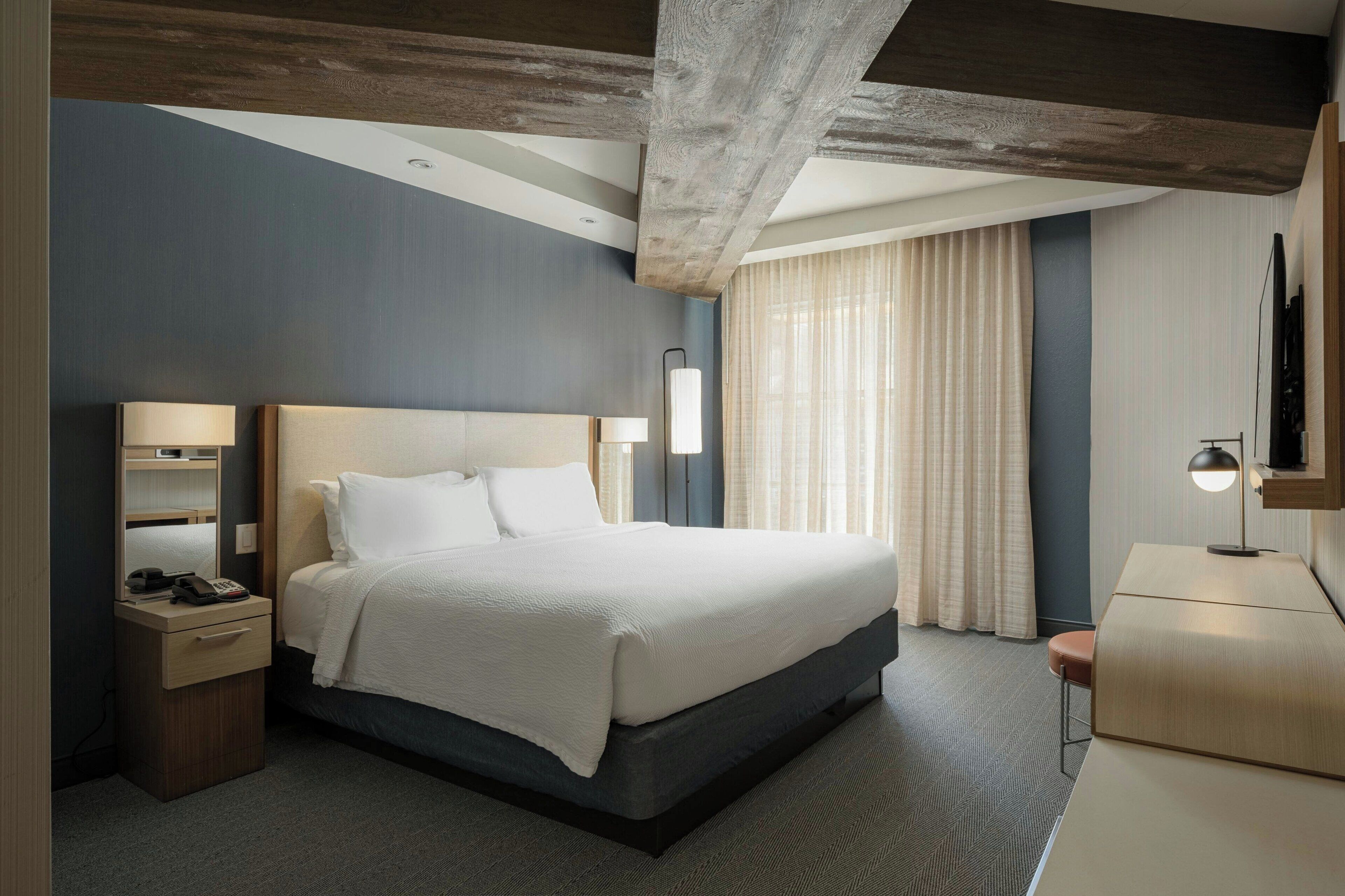 A modern hotel room with a large bed, bedside tables, a desk, and a flat-screen TV.
