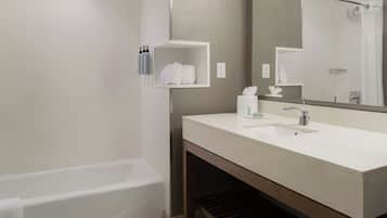 A modern bathroom with a white bathtub, a large mirror, and a vanity with a sink and towel rack.