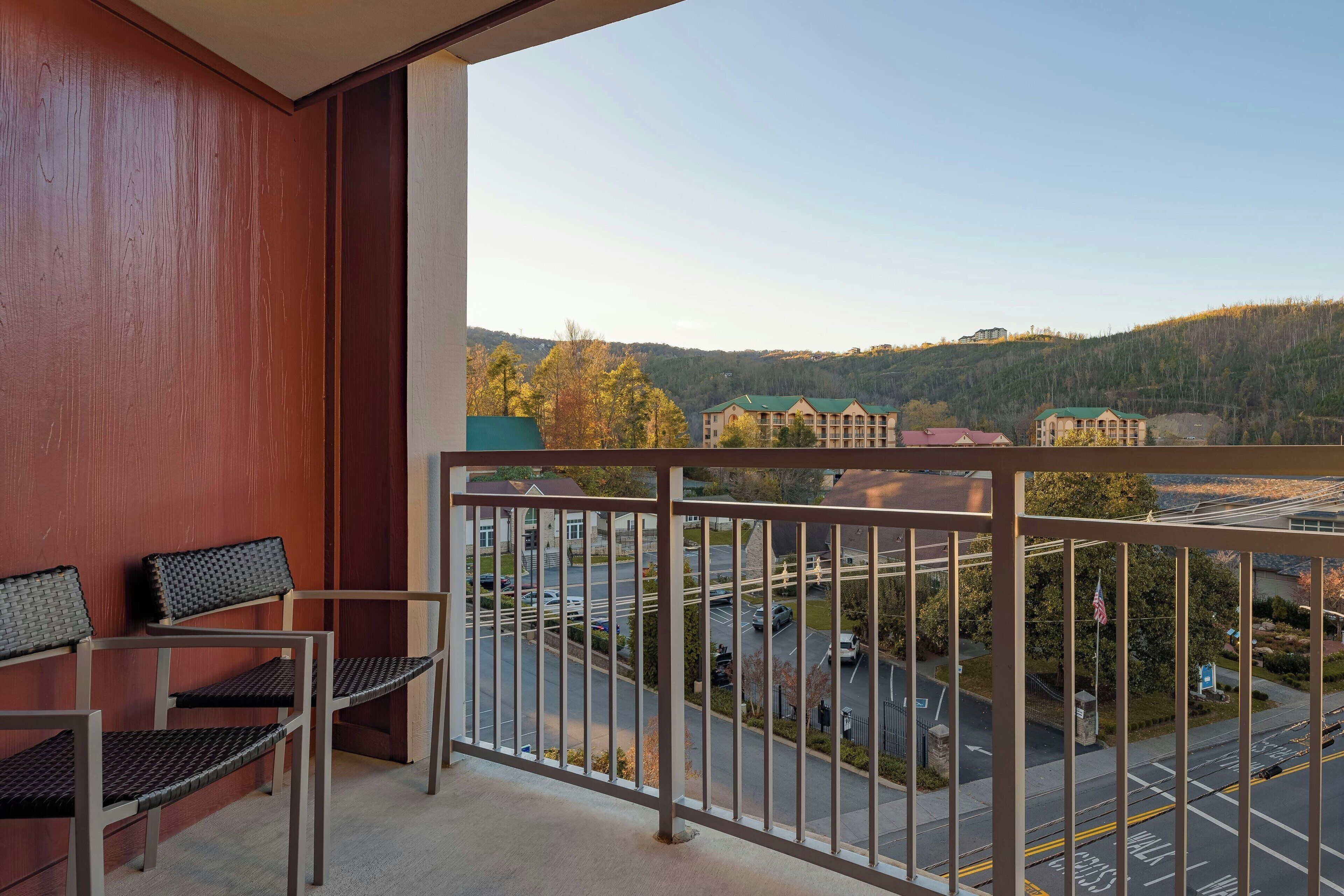 Un balcon donnant sur un parking et sur des bâtiments situés au loin.