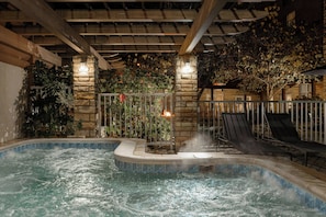 Une piscine intérieure avec un mur en pierre, des chaises longues et un foyer.