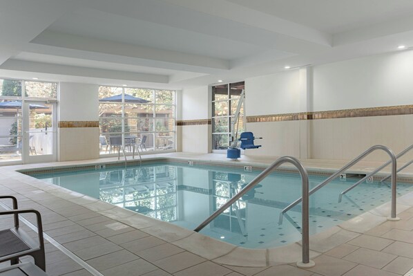 Una piscina interior con agua cristalina, barandales metálicos y suelo de baldosas.