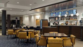 A modern hotel lobby with a seating area, a reception desk, and a digital menu display.