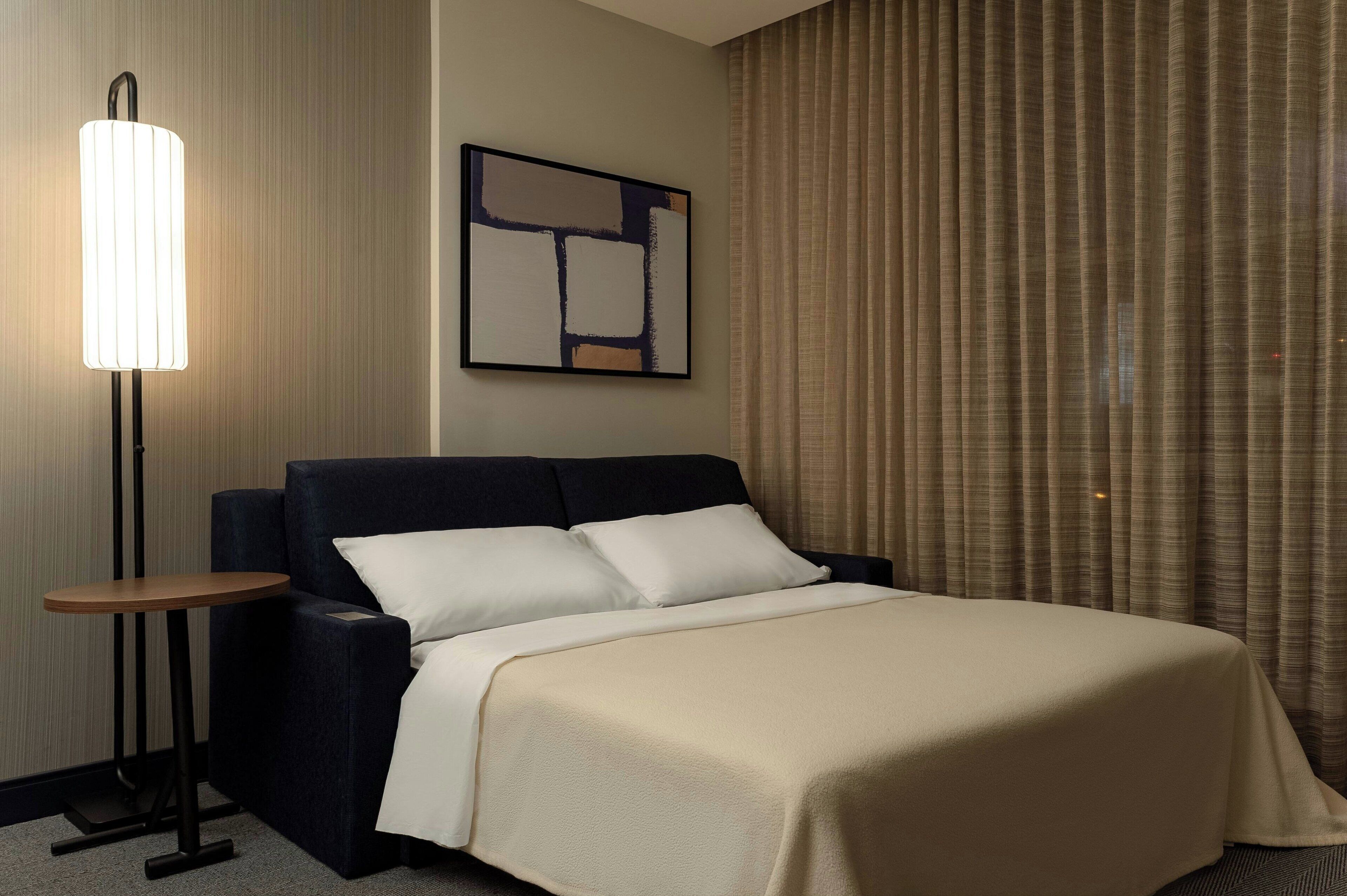 A hotel room with a bed, a bedside table, a lamp, and a painting on the wall.
