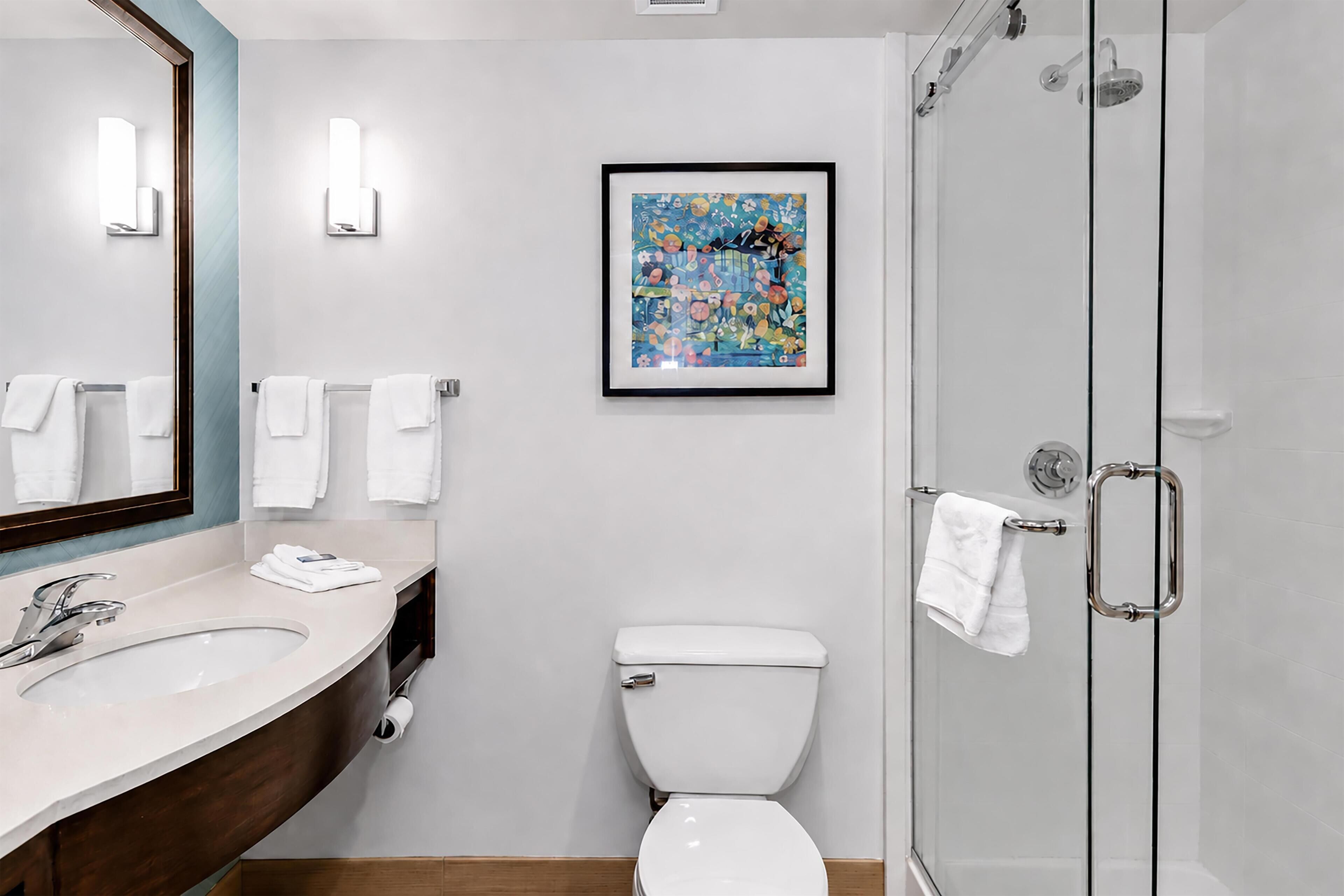 A modern bathroom with a large mirror, a sink, a toilet, and a shower.