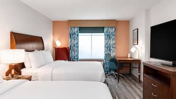 A hotel room with two beds, a desk, a TV, and a window with curtains.