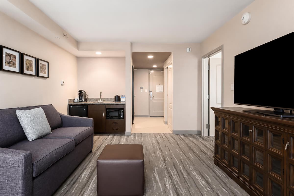 A modern living room with a sofa, ottoman, flat-screen TV, and a wooden cabinet.