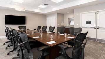 A conference room with a long table, chairs, a flat-screen TV, and a door with a sign.