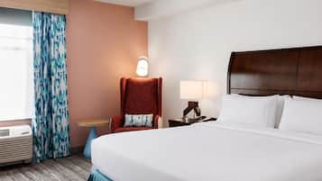 A hotel room with a bed, a chair, a table, a lamp, and a window with curtains.