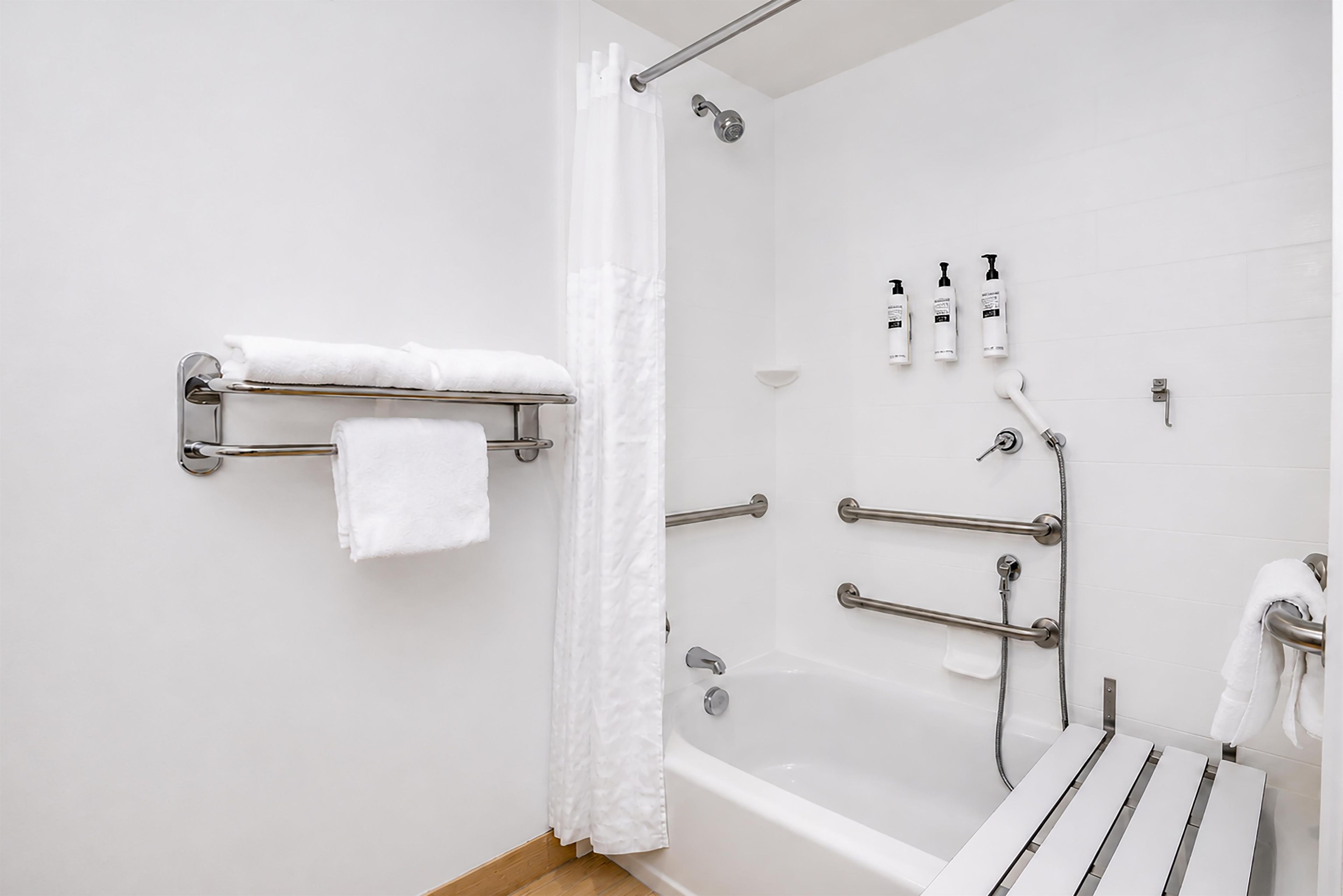 A modern bathroom with a bathtub, shower, and handrails.