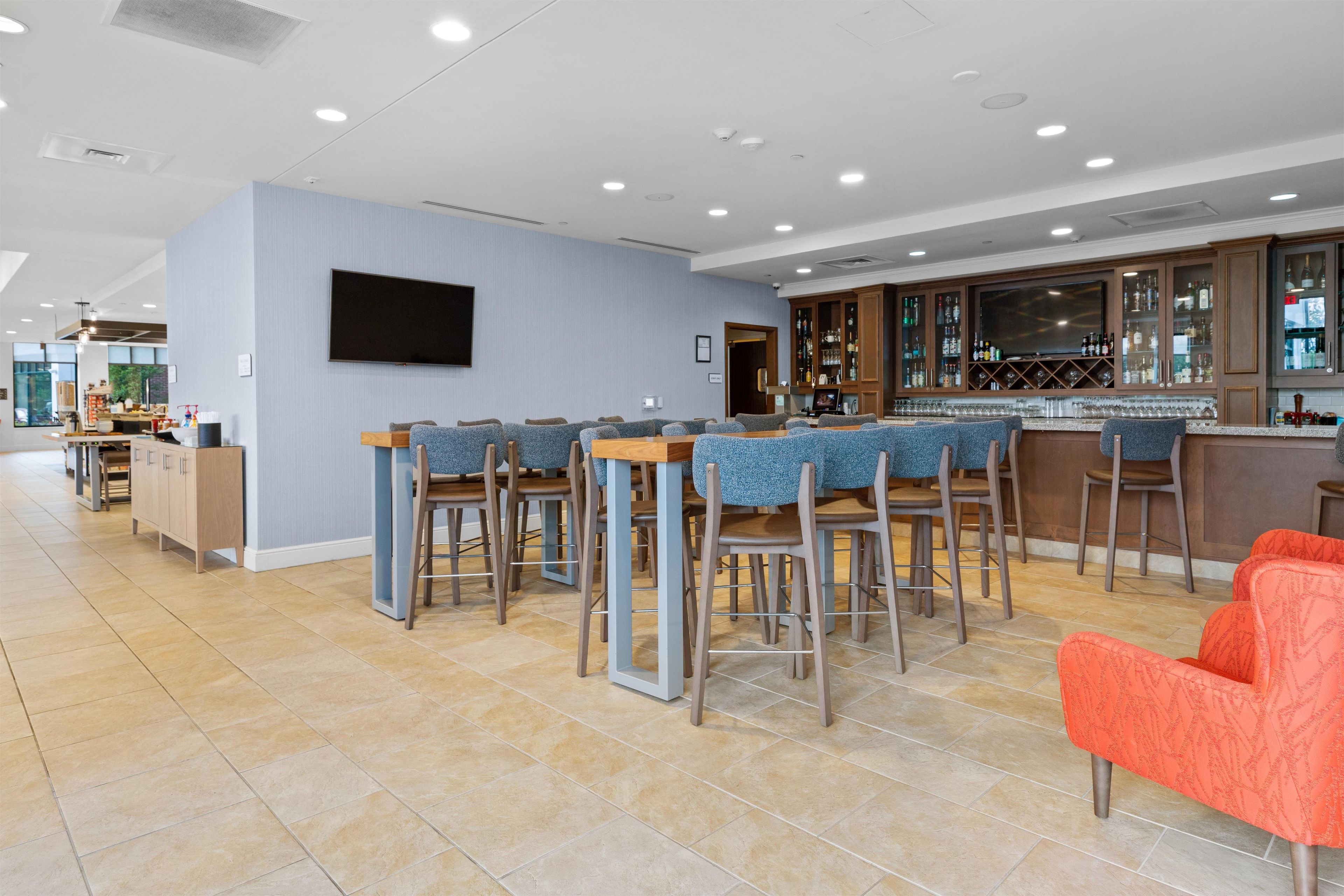 A modern bar area with a long counter, multiple bar stools, and a television mounted on the wall.