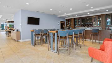 A modern bar area with a long counter, multiple bar stools, and a television mounted on the wall.