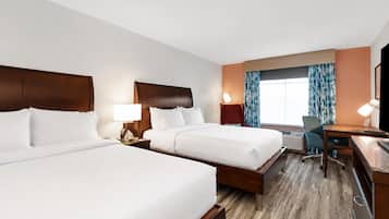 A hotel room with two beds, a desk, a chair, and a TV.