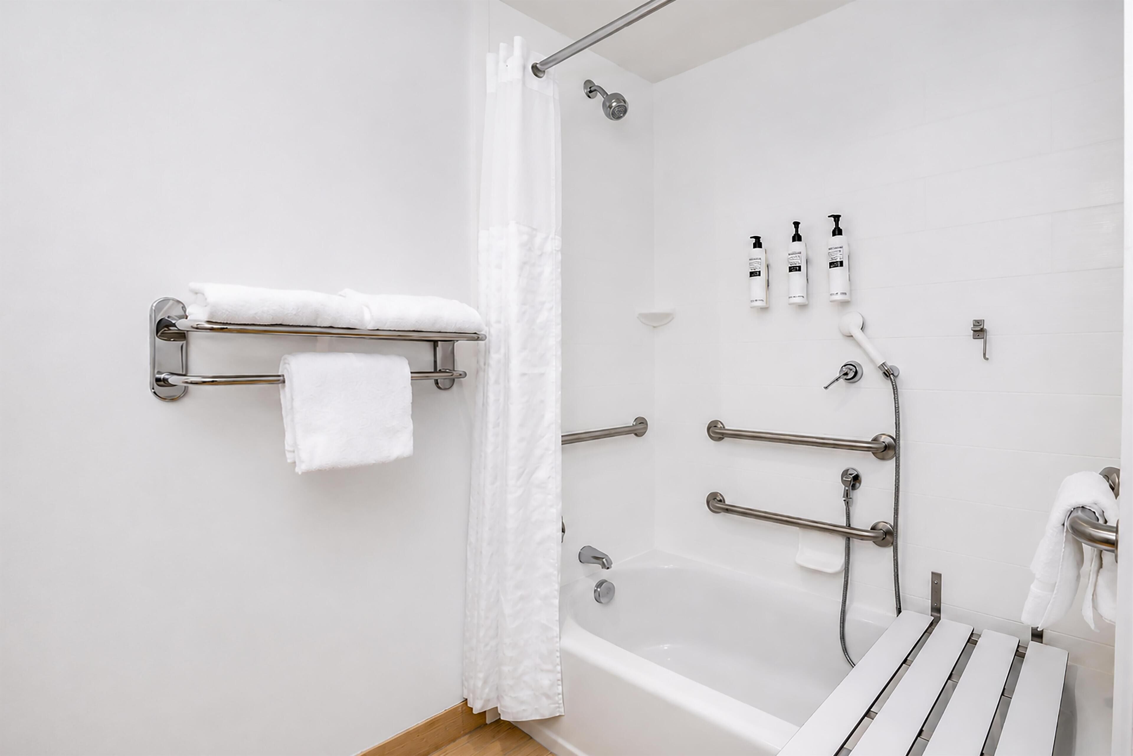 A modern bathroom with a bathtub, shower, and handrails.
