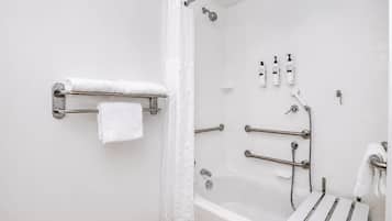 A modern bathroom with a bathtub, shower, and handrails.