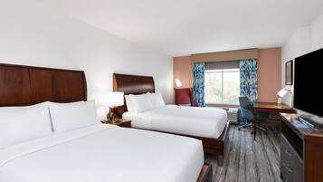 A hotel room with two beds, a desk, a chair, a TV, and a window with curtains.