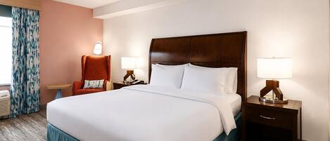 A hotel room with a large bed, two bedside tables with lamps, a chair, and a window with curtains.