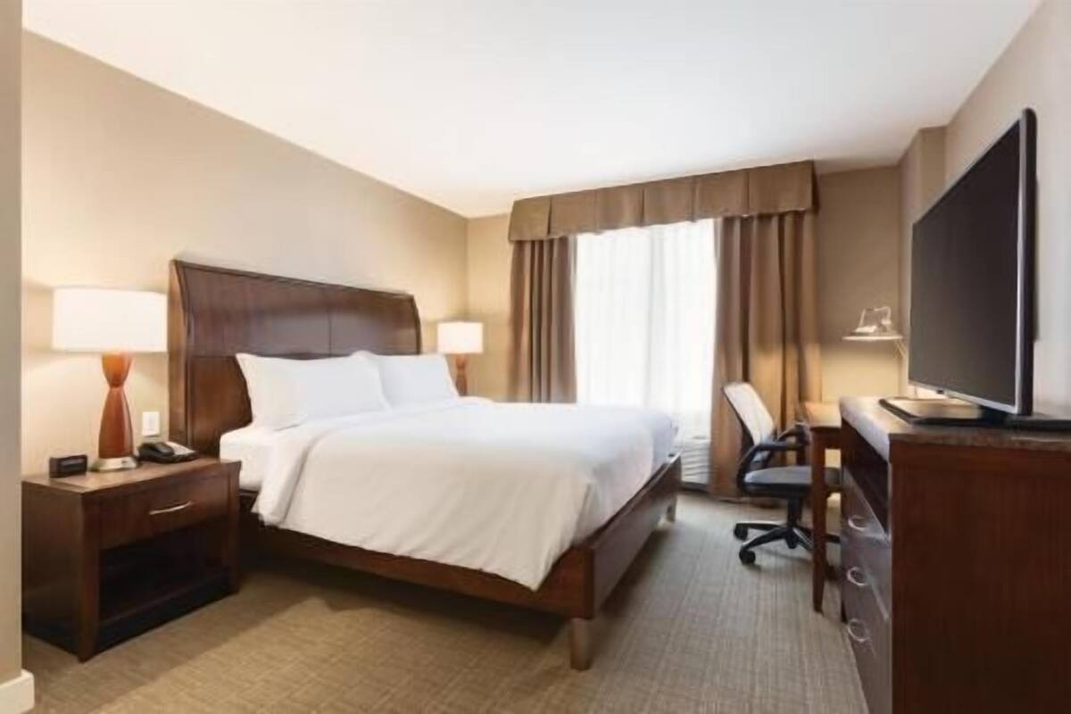 A hotel room with a bed, bedside tables, a desk, a chair, a television, and curtains.