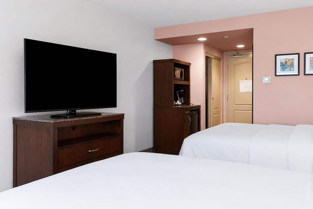 A hotel room with a flat-screen TV on a wooden cabinet, a white bed, and a door leading to a bathroom.