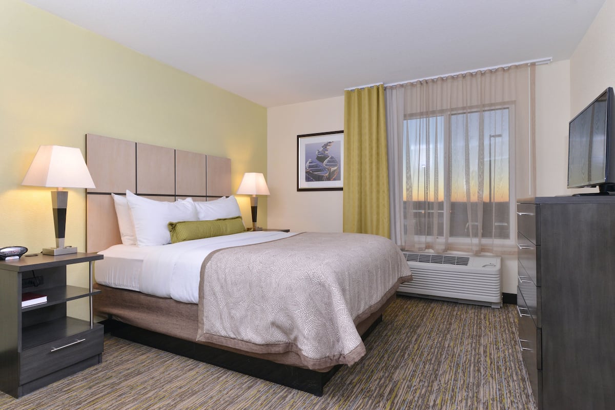 A hotel room with a bed, bedside lamps, a flat-screen TV, a heater, and a window with curtains.