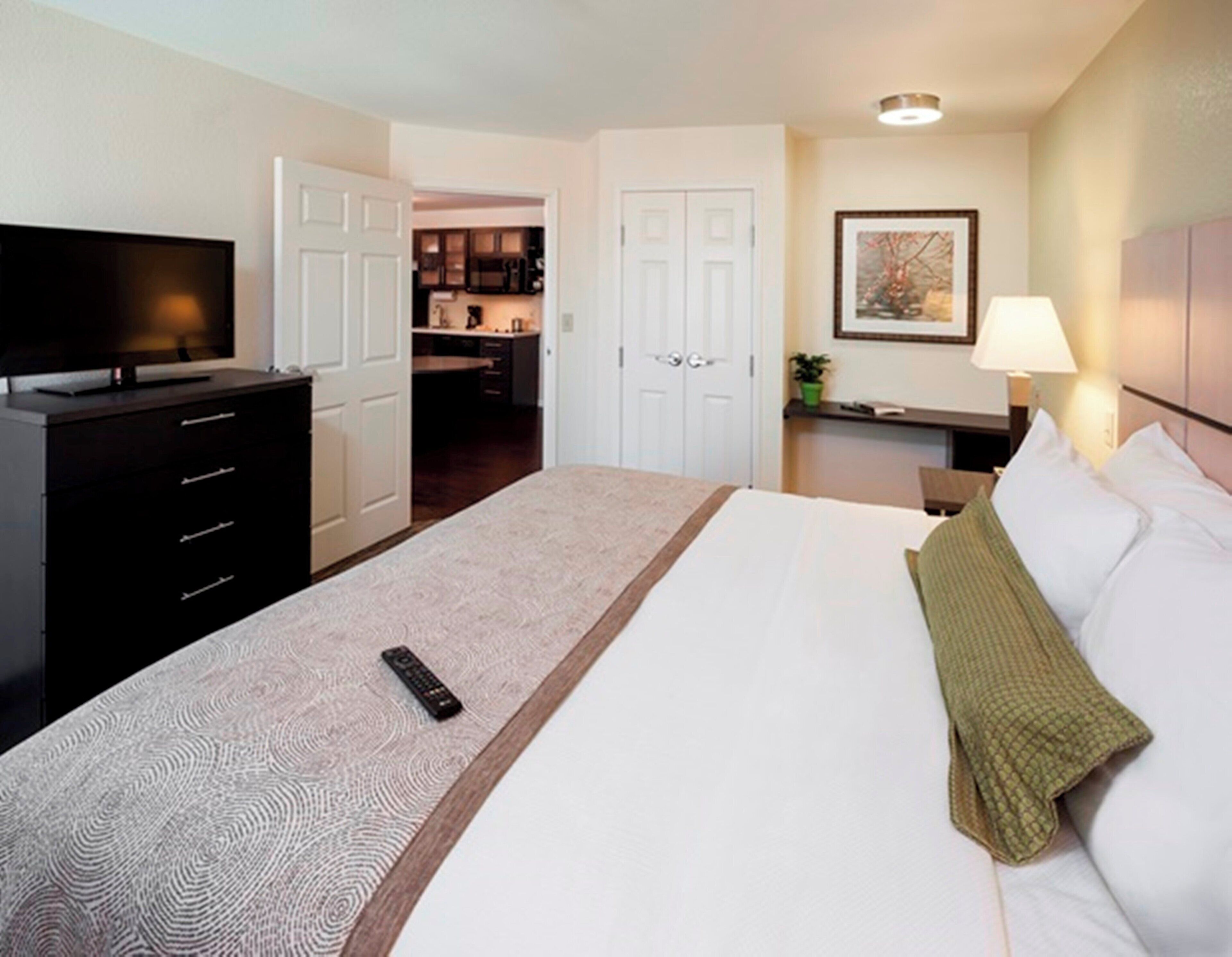 Une chambre d’hôtel avec un lit, une télévision, un bureau et, au fond, une kitchenette.