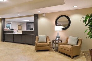 A reception area with a counter, two armchairs, a lamp, and a mirror on the wall. - Candlewood Suites Casper by IHG (Casper)