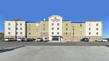 Un hotel con entrada central, varios espacios de estacionamiento y un cielo azul despejado.