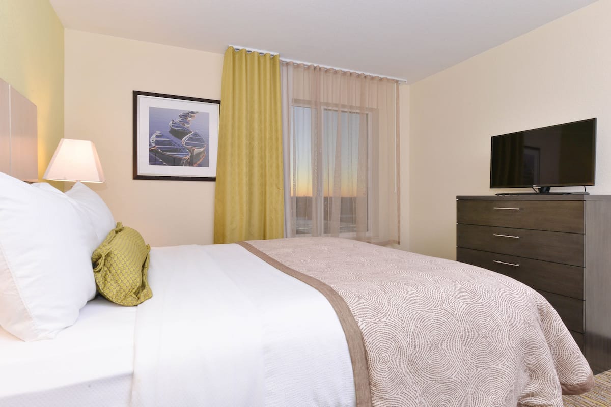 A hotel room with a bed, a television, a dresser, and a window with curtains.