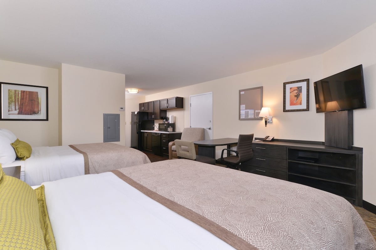 A hotel room with two beds, a desk, a chair, a television, and a kitchenette.
