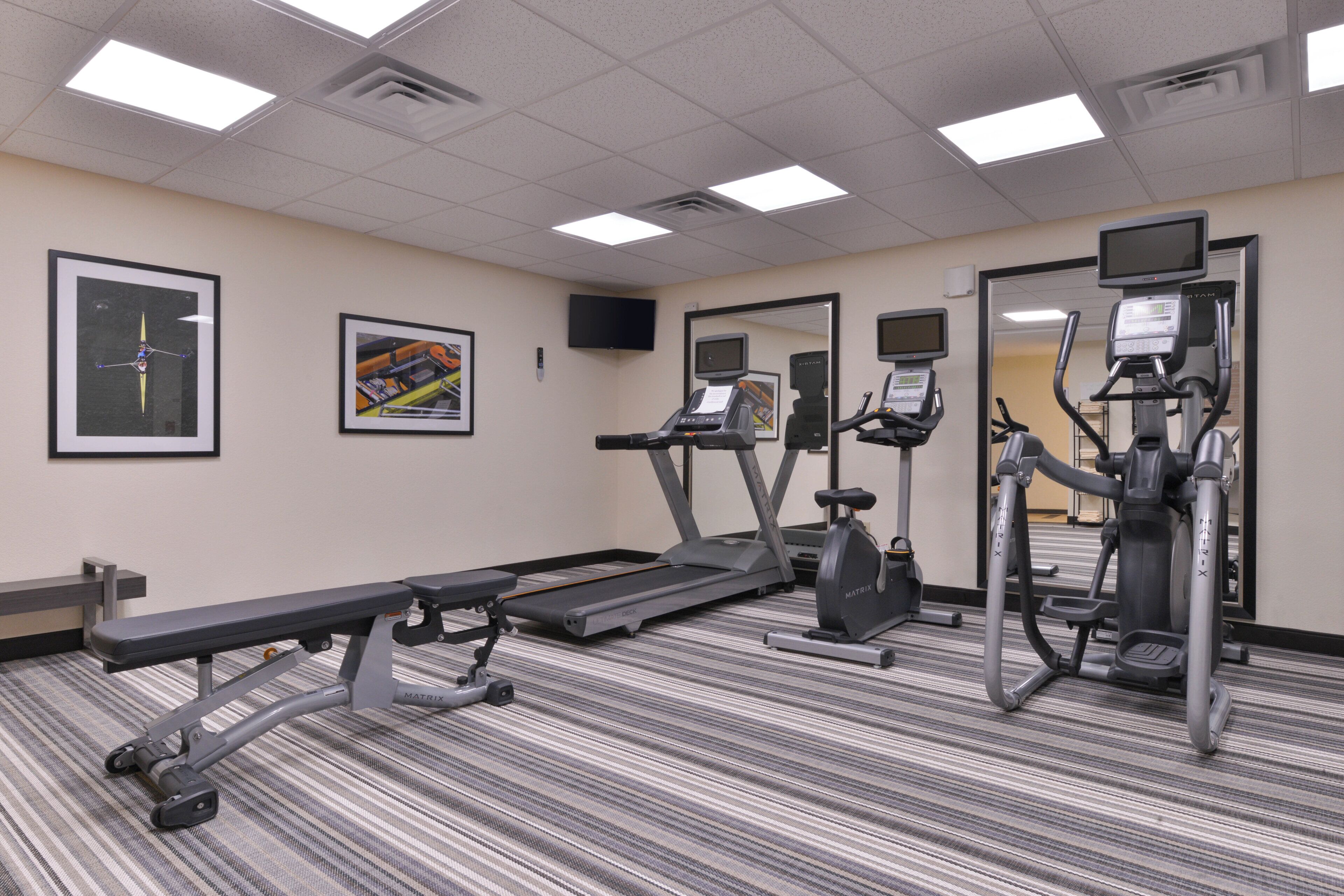 A fitness center with treadmills, elliptical machines, and a bench.
