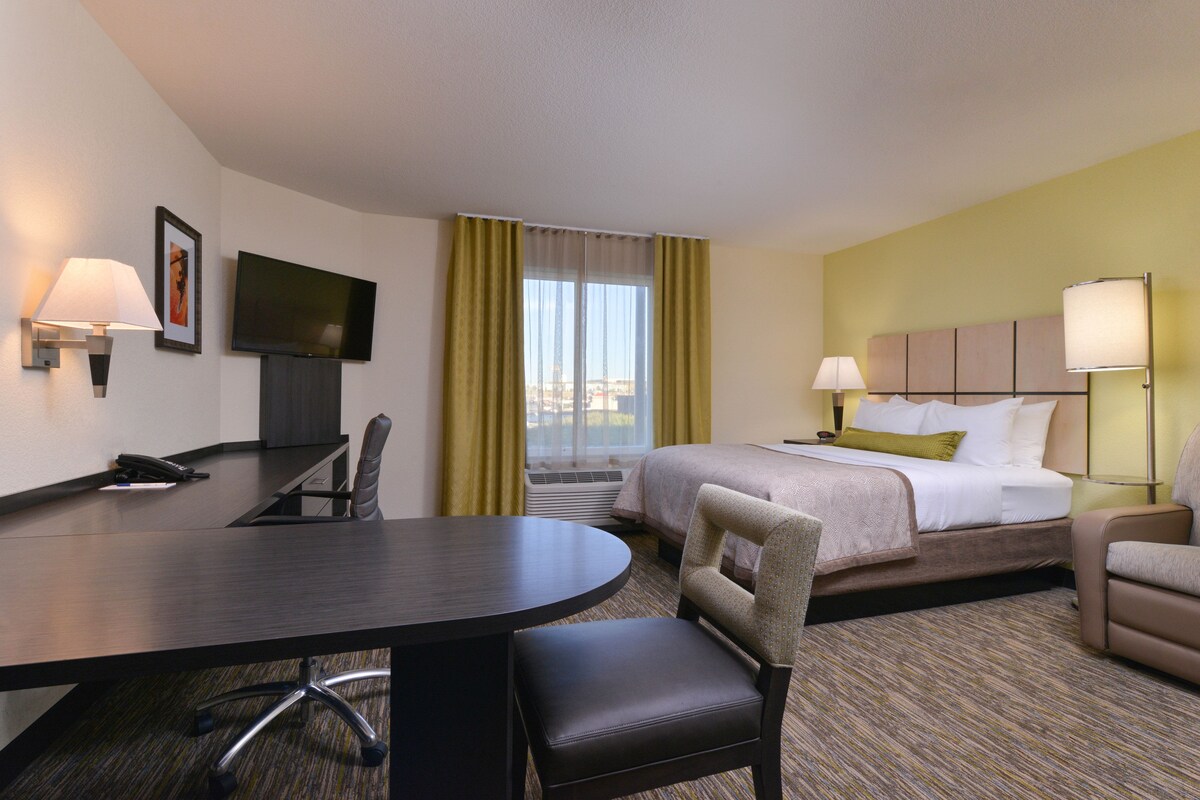 A hotel room with a bed, a desk with a chair, a TV, and a window with curtains.