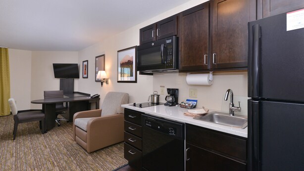 A compact hotel kitchen with a microwave, refrigerator, sink, and a small dining area with a table and chairs. - Candlewood Suites Casper by IHG (Casper)