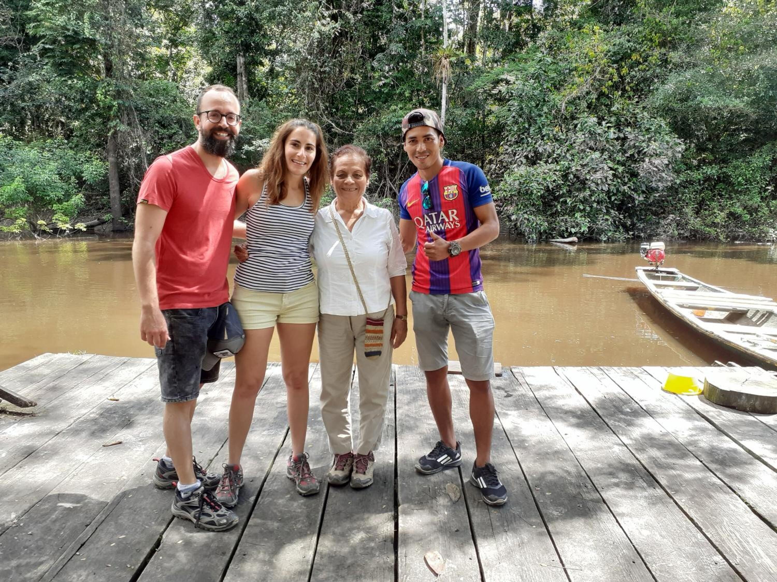 A group of people standing on a wooden dock by a river surrounded by dense greenery.