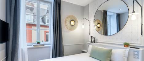 A modern hotel room with a large bed, a round mirror, and a window with curtains.