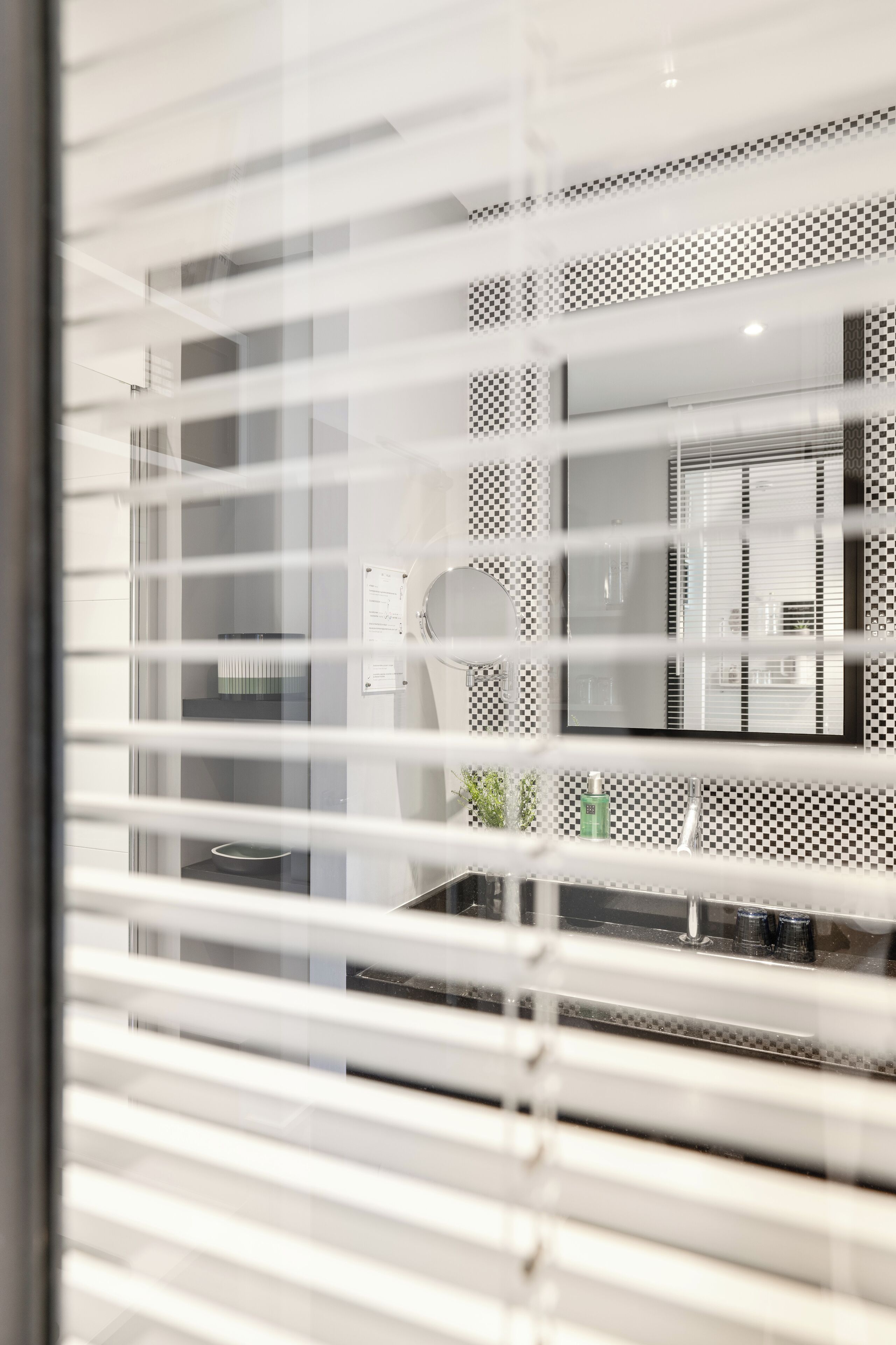 A modern kitchen with a checkered backsplash, a stainless steel sink, and a window with blinds.