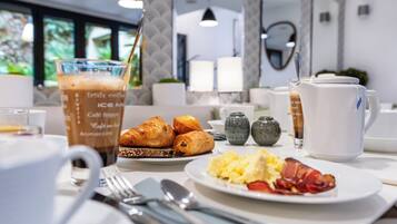 A breakfast table with croissants, scrambled eggs, bacon, and a coffee drink.