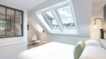 A modern bedroom with a skylight, a bed, a chair, and a lamp.