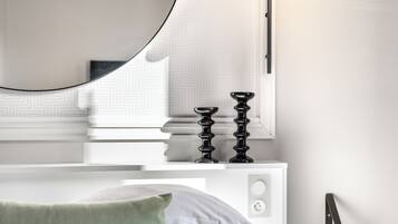 Quarto moderno com um espelho redondo grande, uma mesa de cabeceira com abajur e uma cama com travesseiro verde.