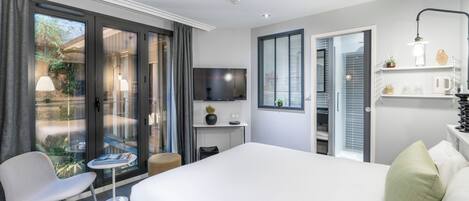 Una habitación de hotel moderna con una cama grande, un espacio de descanso con una pequeña mesa, un televisor y un balcón con cortinas.