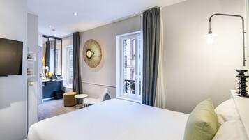 A modern hotel room with a large bed, a small desk, a chair, a TV, and a window with curtains.