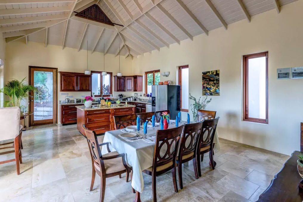 A spacious kitchen with wooden cabinets, a dining area with a table set for six, and a large window providing natural light.