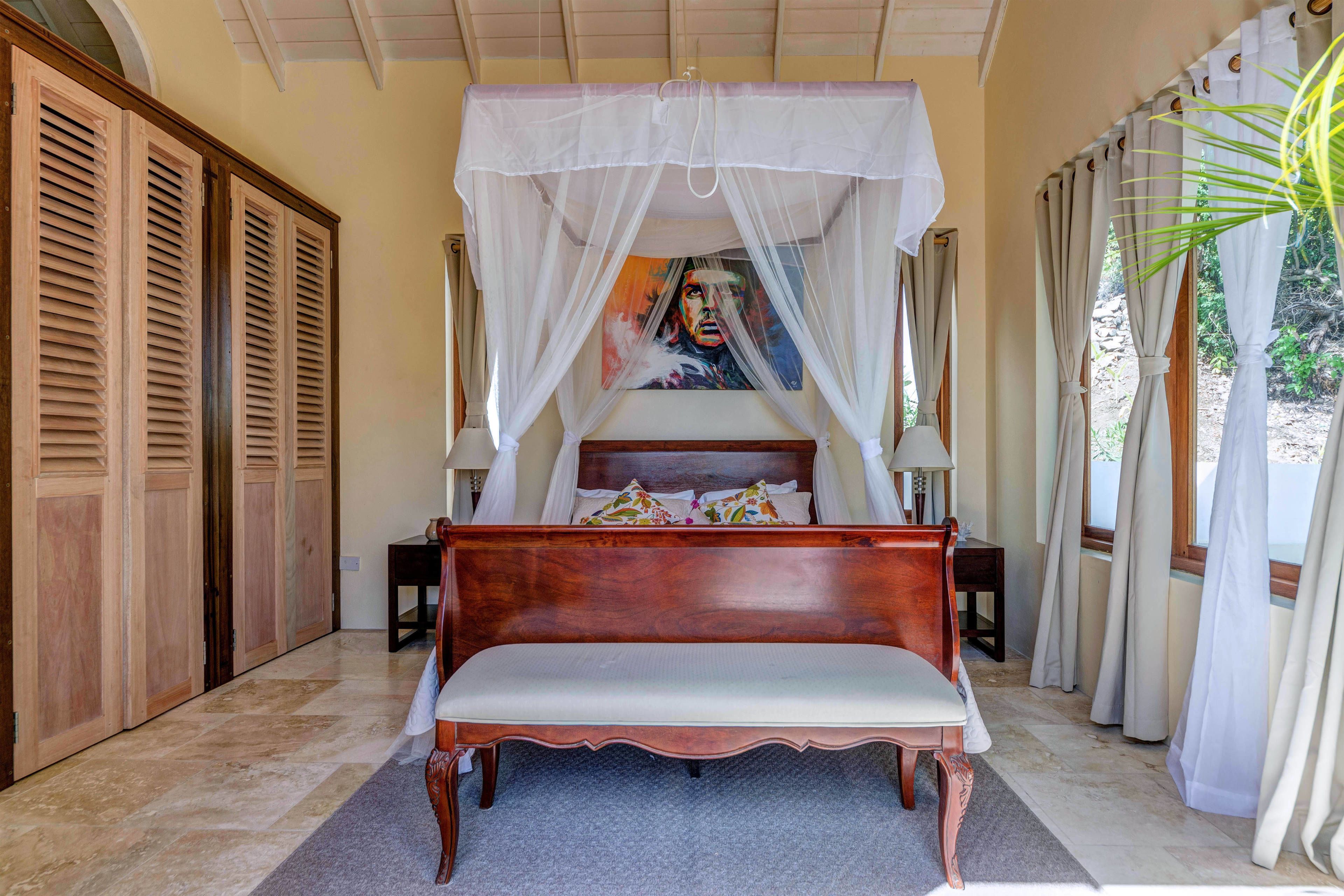 A bedroom with a wooden bed, a canopy, a painting on the wall, and a view of the outdoors.