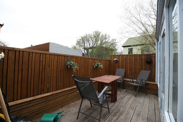 A wooden deck with a table and chairs, a wooden fence, and a window.