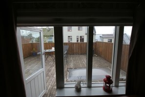 A view through a window of a wooden deck with a table and chairs, a small plant, and a red lantern.